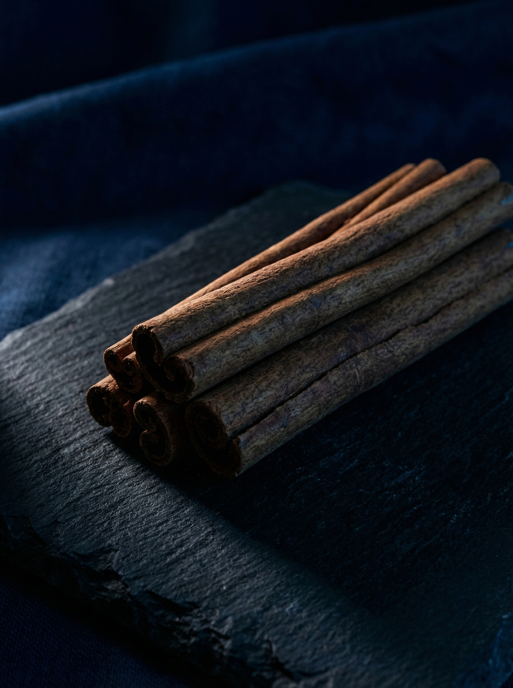 Top note ingredient of Valeria Bless Code of the Heart Homme perfume — cinnamon sticks on dark blue slate stone surface