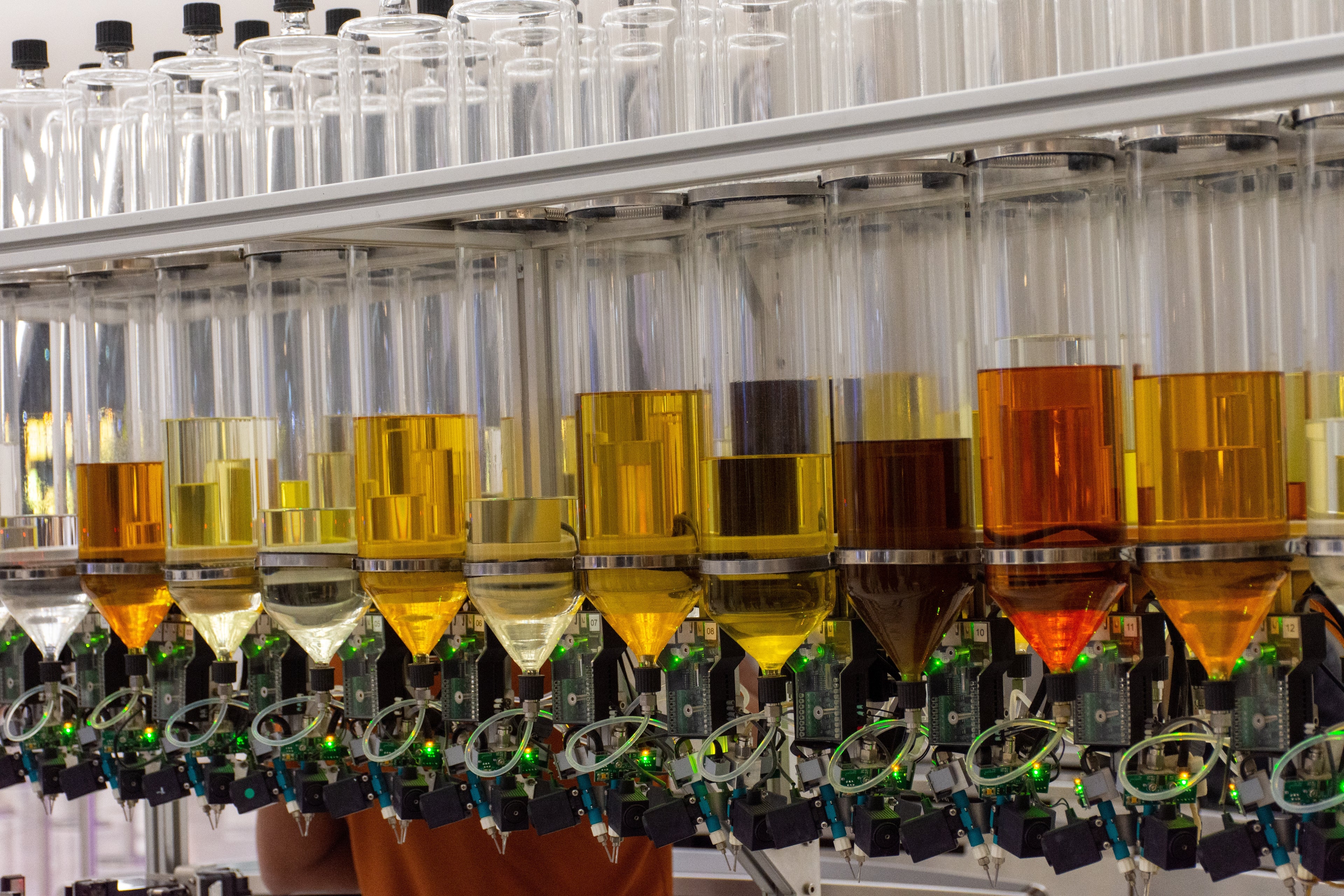 Valeria Bless Perfume laboratory fragrance blending machine with rows of glass containers filled with golden amber and brown aromatic oils and essential extracts